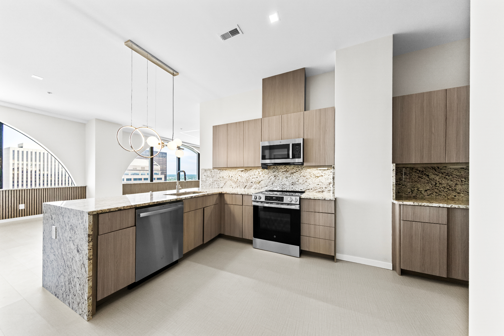 Modern high-rise kitchen with light oak cabinetry, granite countertops, stainless appliances, and ring pendant lighting